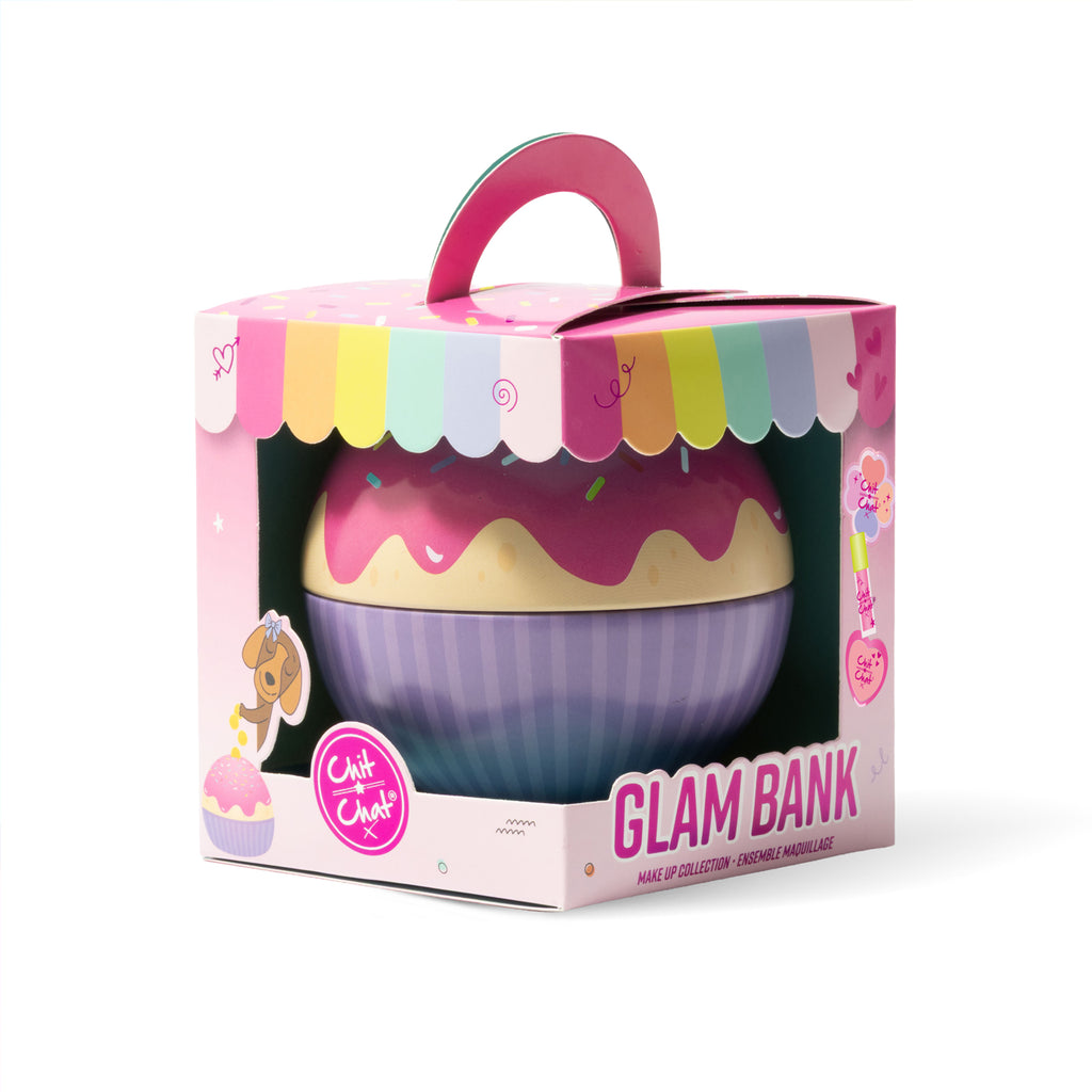 A cupcake-shaped money tin in pink packaging, shown on a clean white background. The box features a handle and a clear window revealing the cupcake design with pink frosting on top and a purple-striped base.