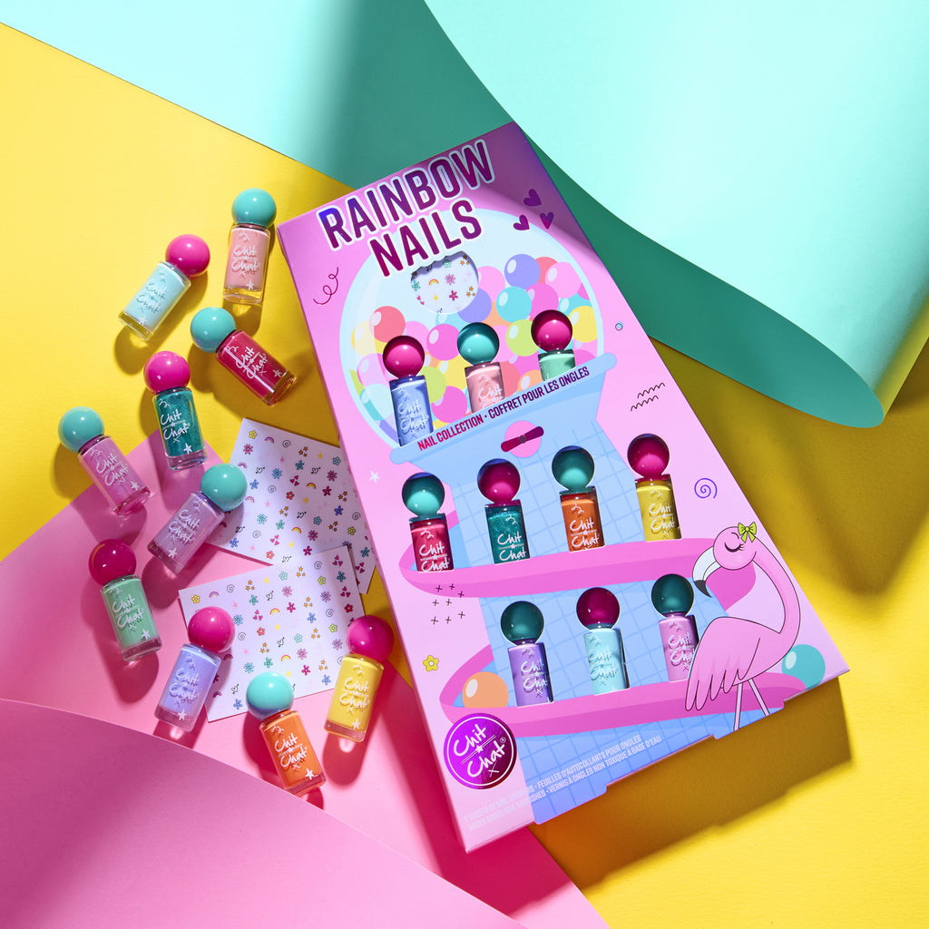 A colourful nail polish set in a pink packaging labelled 'RAINBOW NAILS' by Chit Chat, displayed with several small nail polish bottles and decorative sticker sheets on a bright yellow and pink background with teal paper folds.