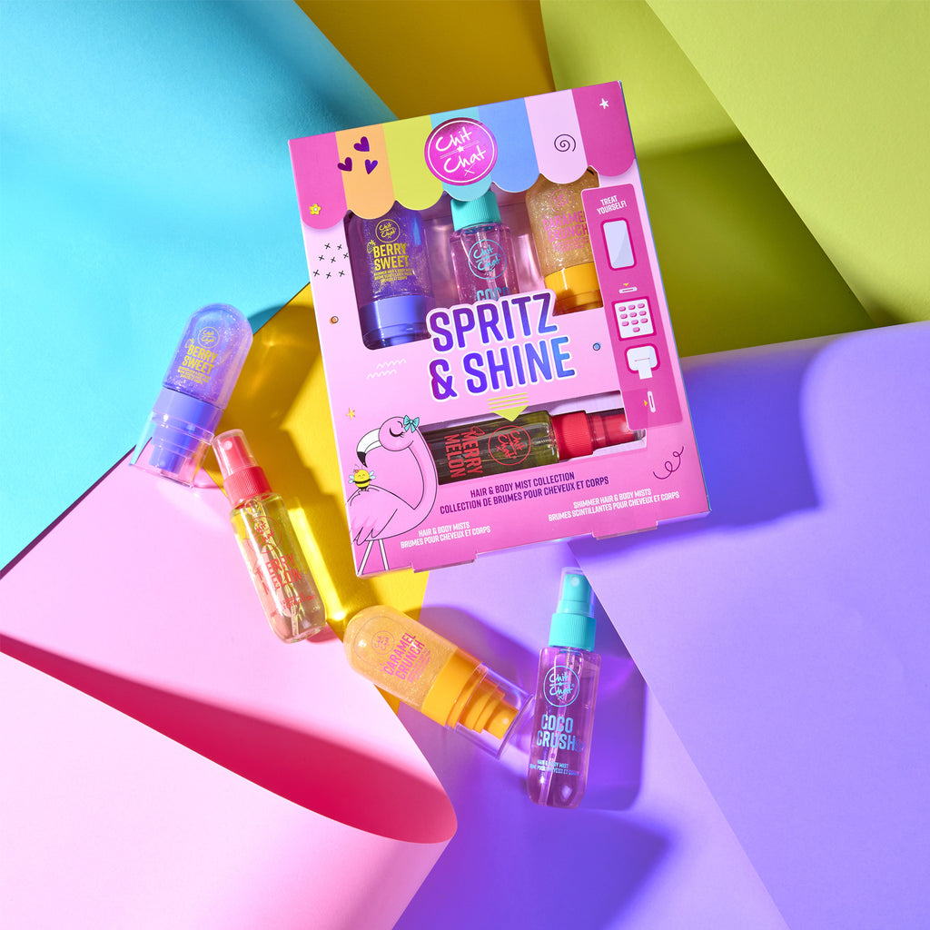A colourful 'Spritz & Shine' collection of travel spray bottles displayed on a vibrant, geometric background of pink, yellow, green, and purple paper.