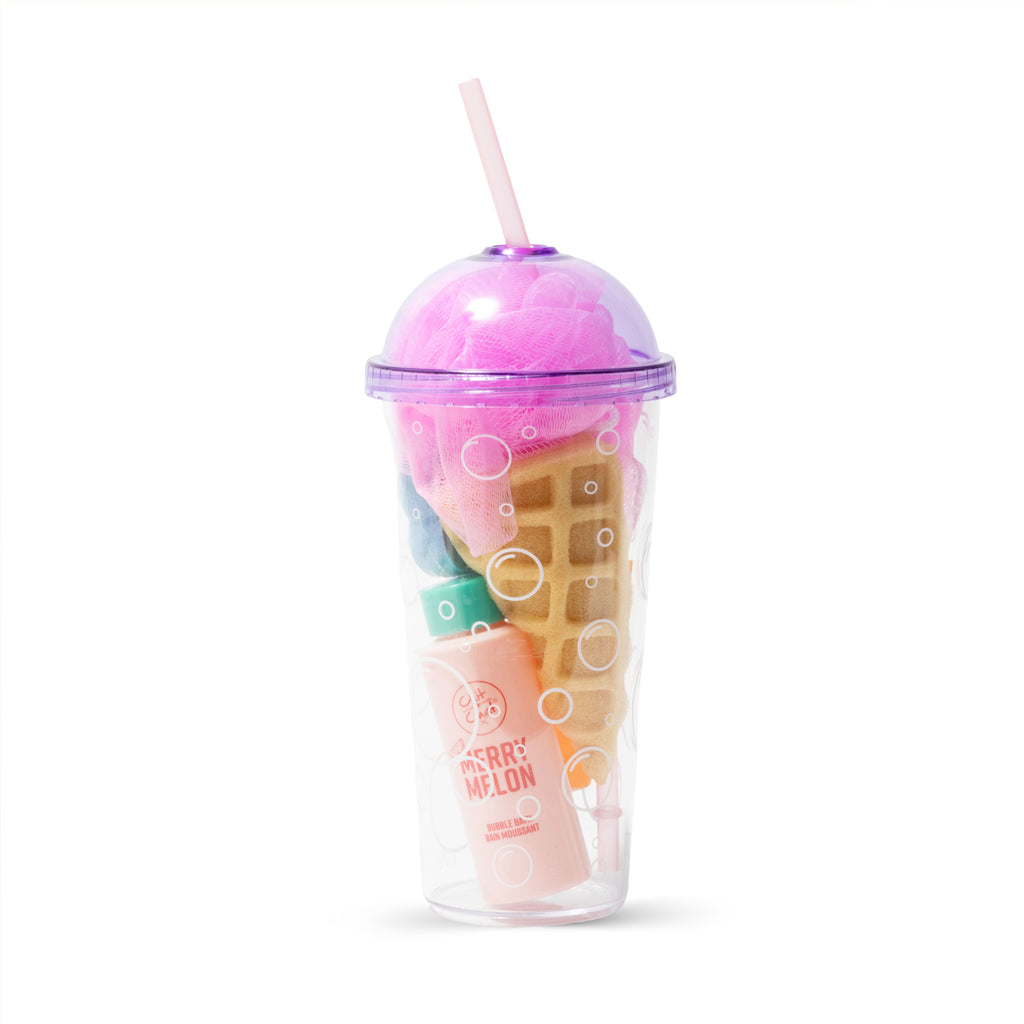 A clear plastic beverage cup with a straw, filled with a waffle-shaped sponge, and a pink shower puff, two bottled bath products and a flower shaped bath fizzer. 