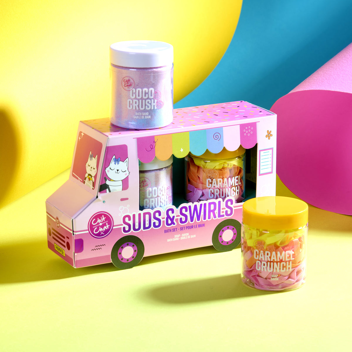 A colourful gift set featuring a pink cardboard truck-shaped box labelled 'Suds & Swirls' with two tubs of bath products. One jar has a white lid and is labelled 'Coco Crush,' and the other has a yellow lid and is labelled 'Caramel Brunch.