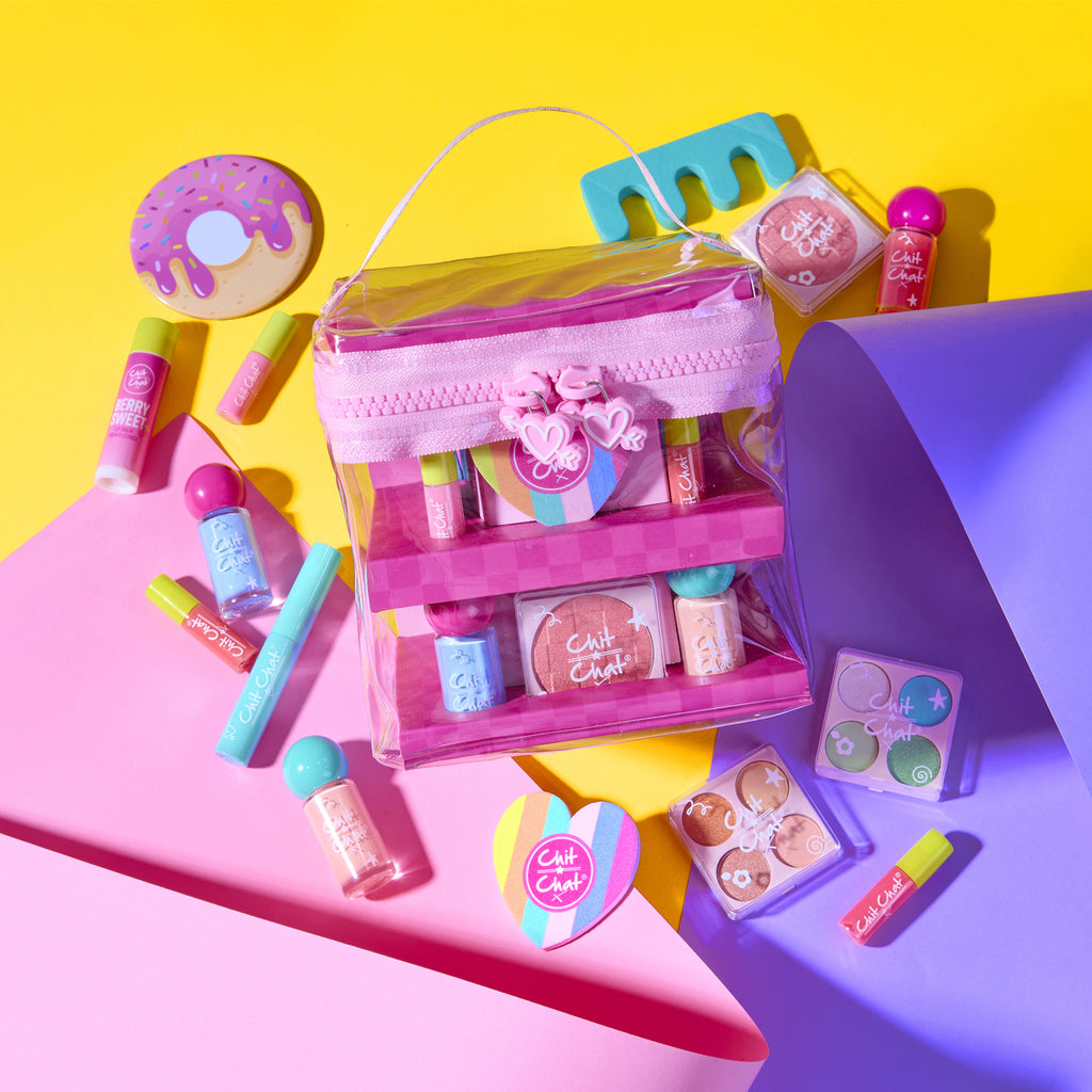 A clear plastic cosmetic bag with a pink heart shaped zip filled with a variety of cosmetics, stacked and displaying on two tiers. With the cosmetics also scattered around the outside of the bag for visibility of the cosmetic products on a colourful background, 