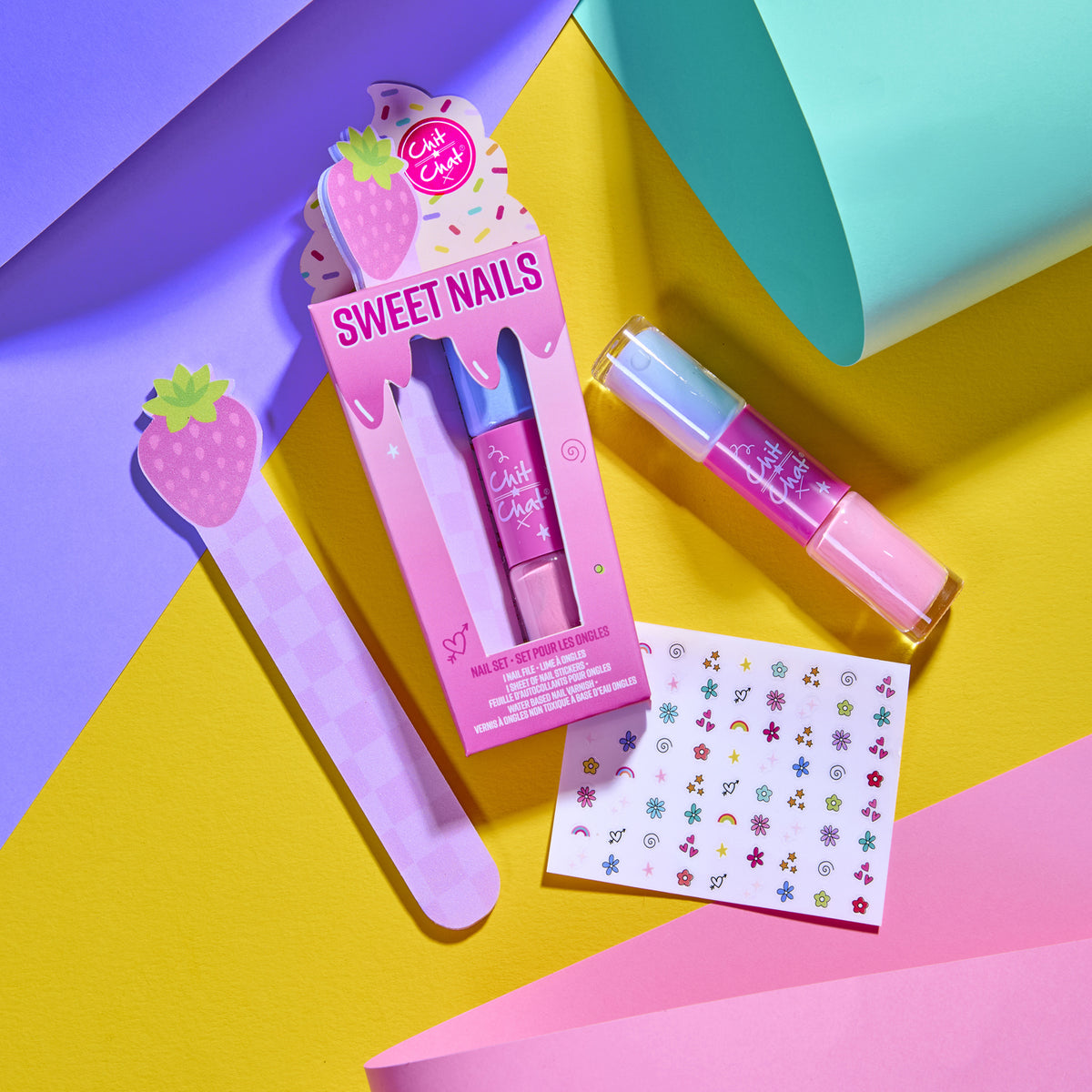 A colorful nail kit named Sweet Nails, featuring a strawberry-shaped nail file, a pink and lilac double ended nail polish tube, a sheet of multi-colour stickers, arranged on a vibrant geometric background.