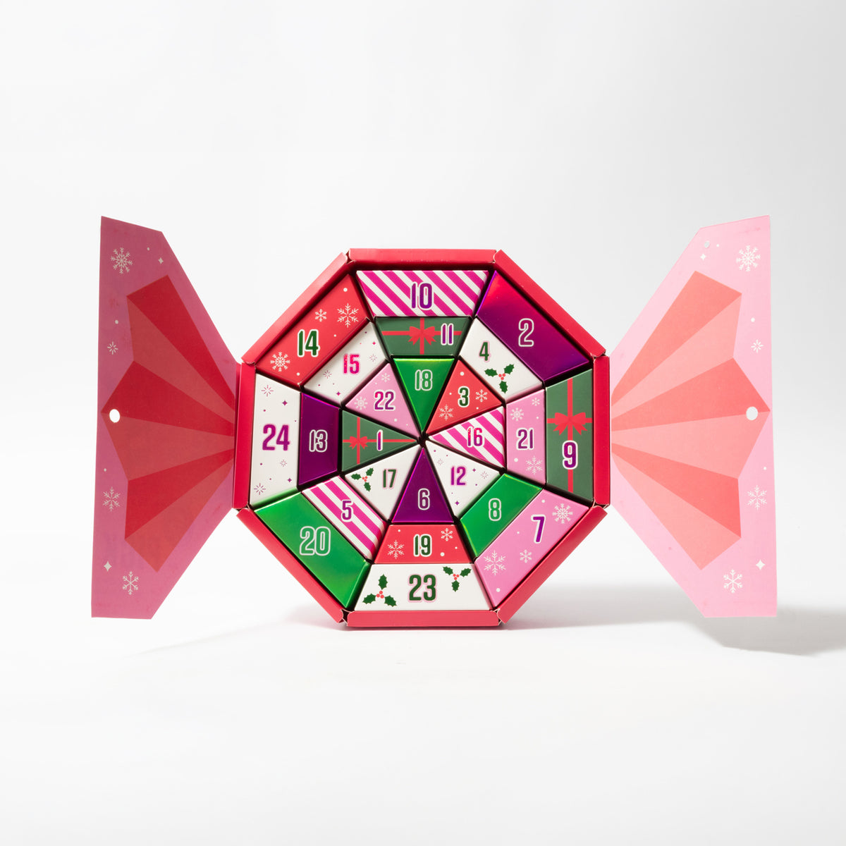 A colourful advent calendar shaped like a candy sweet, with pink and red outer flaps and numbered compartments in the centre, photographed on a clean white background.